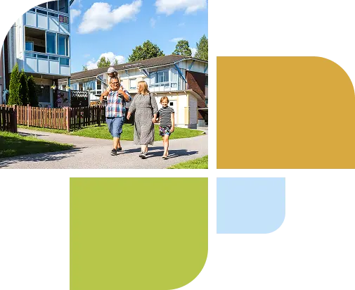 En familj med tre personer går längs en väg framför hus.